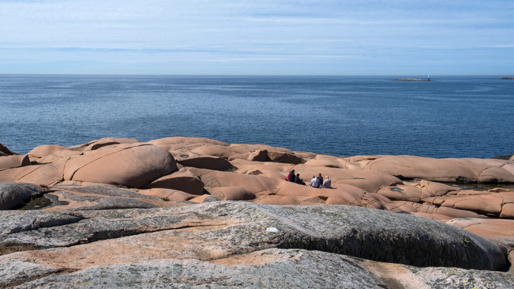 En grupp personer sitter och fikar på rosa klippor. Foto.