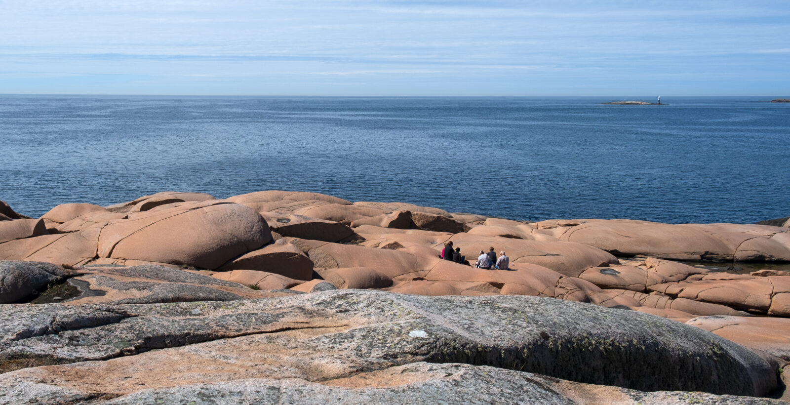 En grupp personer sitter och fikar på rosa klippor. Foto.